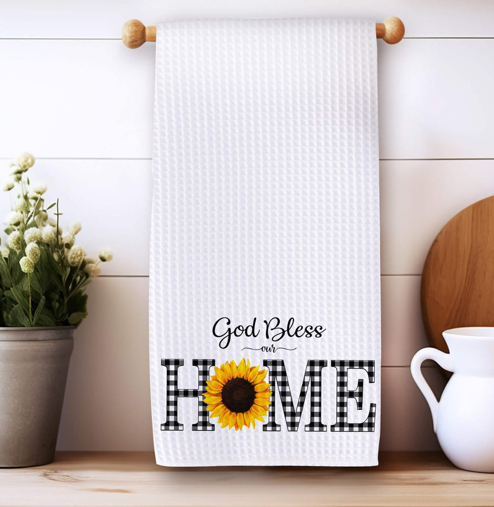 God Bless Our Home kitchen towel with buffalo plaid lettering and a sunflower accent, perfect for farmhouse decor, rustic kitchen accessories, and faith-inspired home gifts - Personalized Kreation