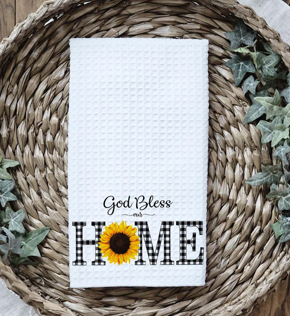 God Bless Our Home kitchen towel with buffalo plaid lettering and a sunflower accent, perfect for farmhouse decor, rustic kitchen accessories, and faith-inspired home gifts - Personalized Kreation