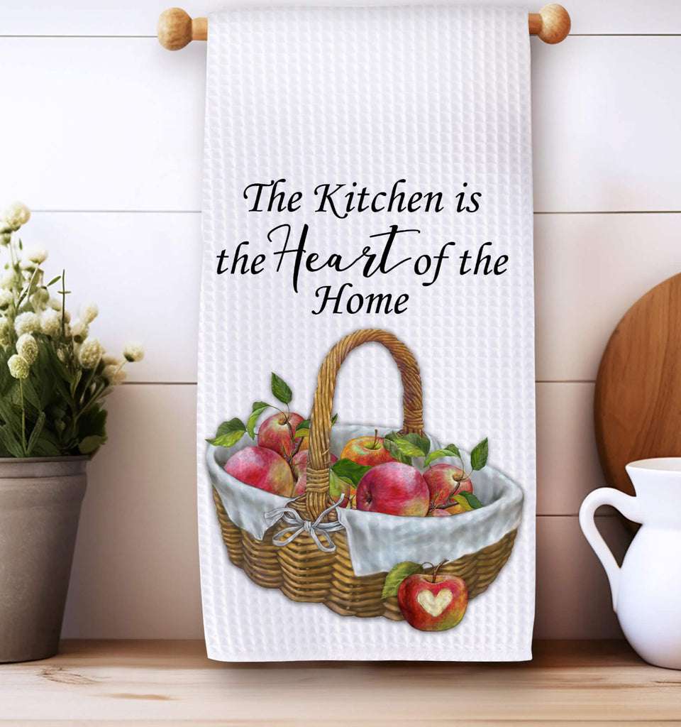 Rustic farmhouse kitchen towel featuring a woven basket filled with fresh red apples adorned with a white linen cloth and a heart The towel reads The Kitchen is the Heart of the Home making it a charming addition to any country kitchen or cozy home - Personalized Kreation