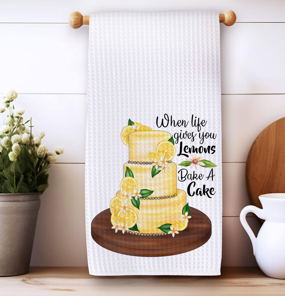 Lemon Cake Kitchen Towel - A beautifully designed white tea towel featuring a vibrant lemon-adorned cake with the phrase 'When Life Gives You Lemons, Bake A Cake.' Perfect for farmhouse decor, baking lovers, and unique kitchen gifts