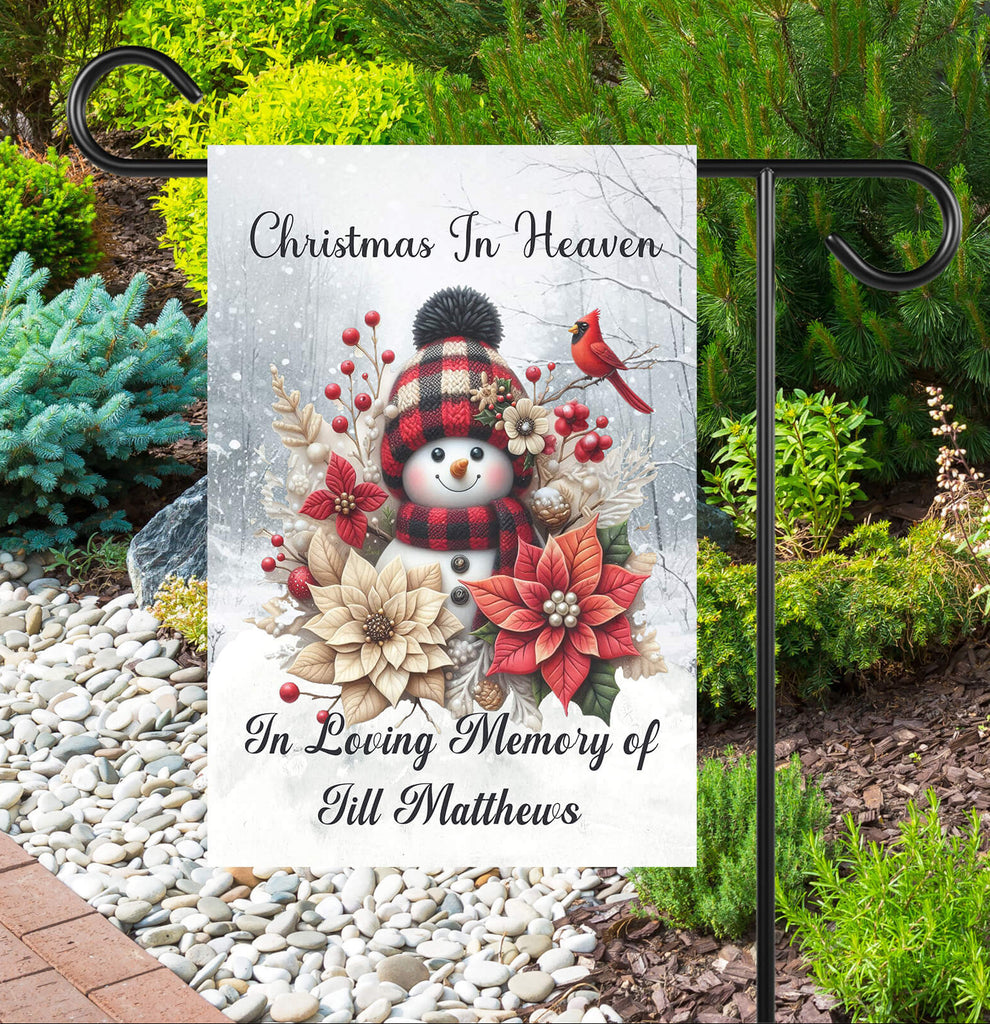 Memorial garden flag with snowman, flowers, and text 'Christmas In Heaven' in a garden setting.