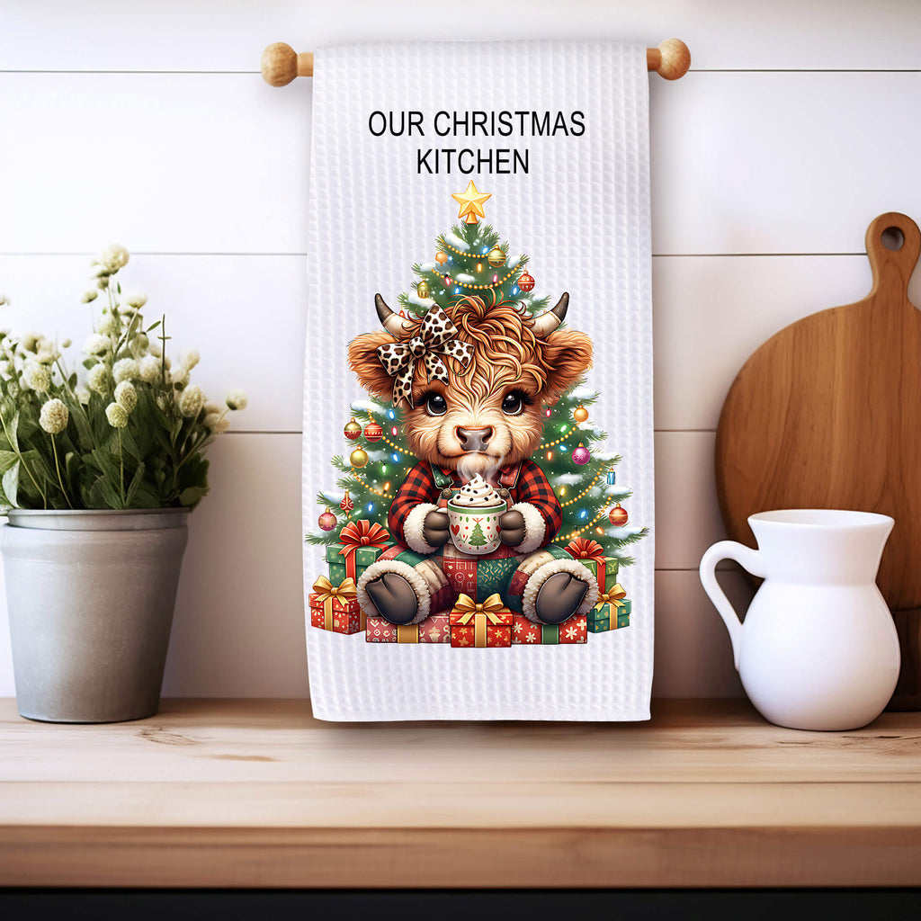 Kitchen towel with a Christmas design featuring a cow and tree, placed on a wooden surface.
