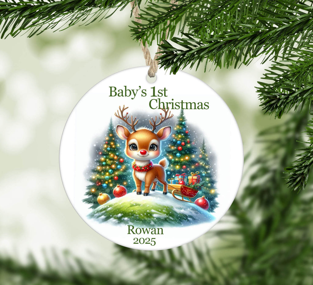 Christmas ornament with a reindeer and Christmas tree, featuring 'Baby's 1st Christmas' text, hanging on a tree.