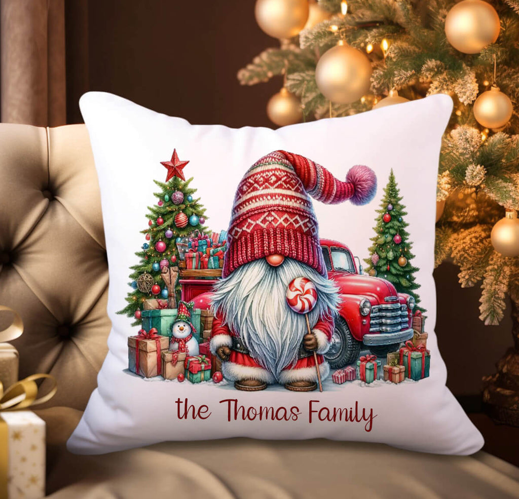 Decorative pillow with Christmas design featuring a gnome and truck, placed on a couch with a tree in the background.