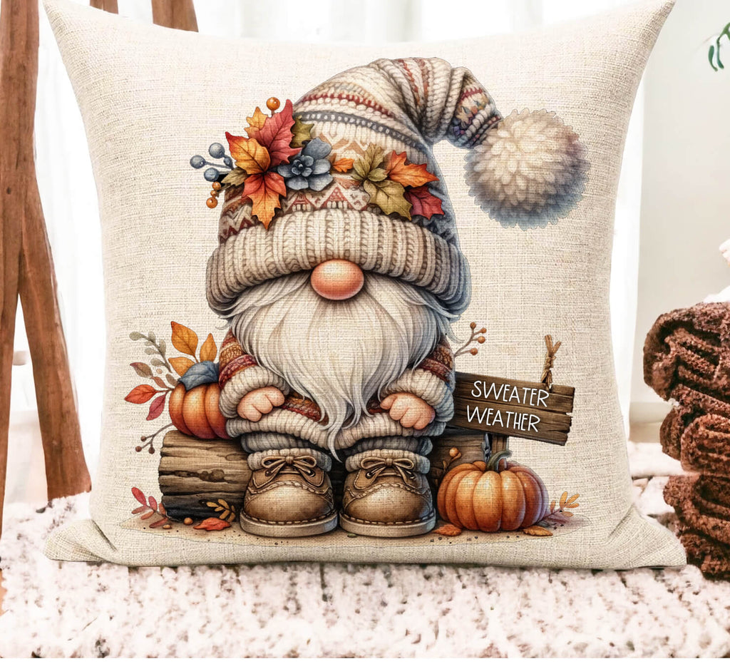 Decorative pillow with a gnome illustration and 'Sweater Weather' sign, surrounded by pumpkins and autumn leaves.