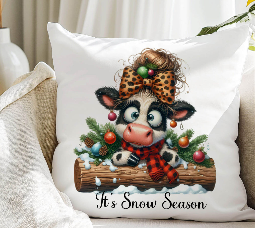 Decorative pillow with a cow illustration and 'It's Snow Season' text, placed on a couch.