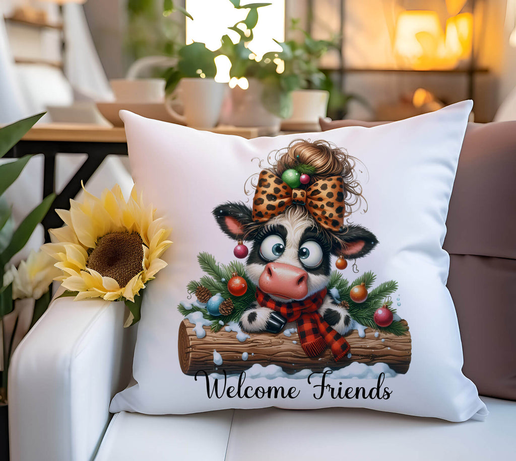 Decorative pillow with a cartoon cow wearing a bow and sitting on a log, surrounded by Christmas decorations, on a couch.