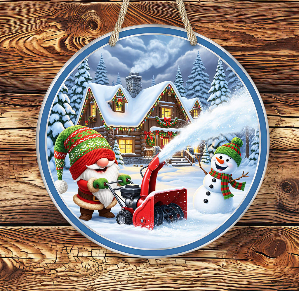 Decorative plate with a winter scene featuring a gnome and snowman using a snow blower, hanging on a wooden surface.