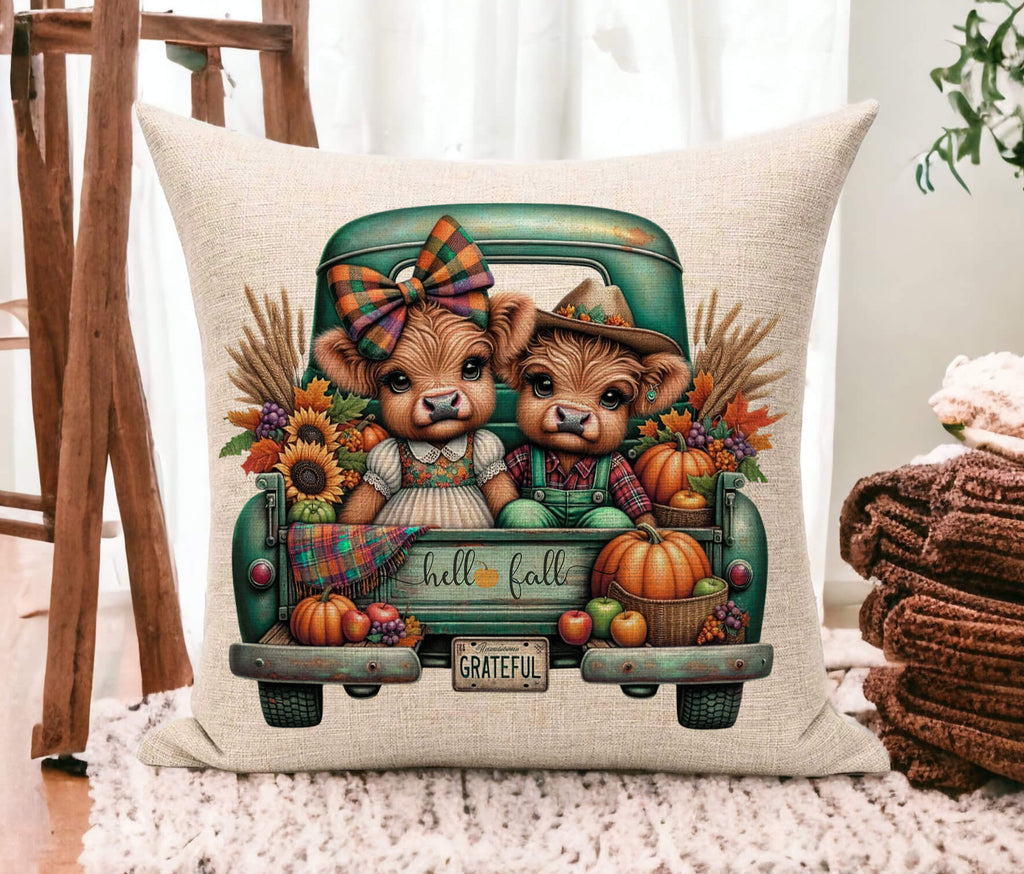 Decorative pillow with highland cows in a truck and fall-themed design on a surface.
