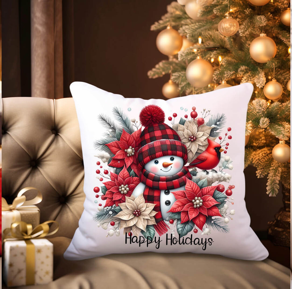 Decorative pillow with a snowman and festive design in front of a Christmas tree.