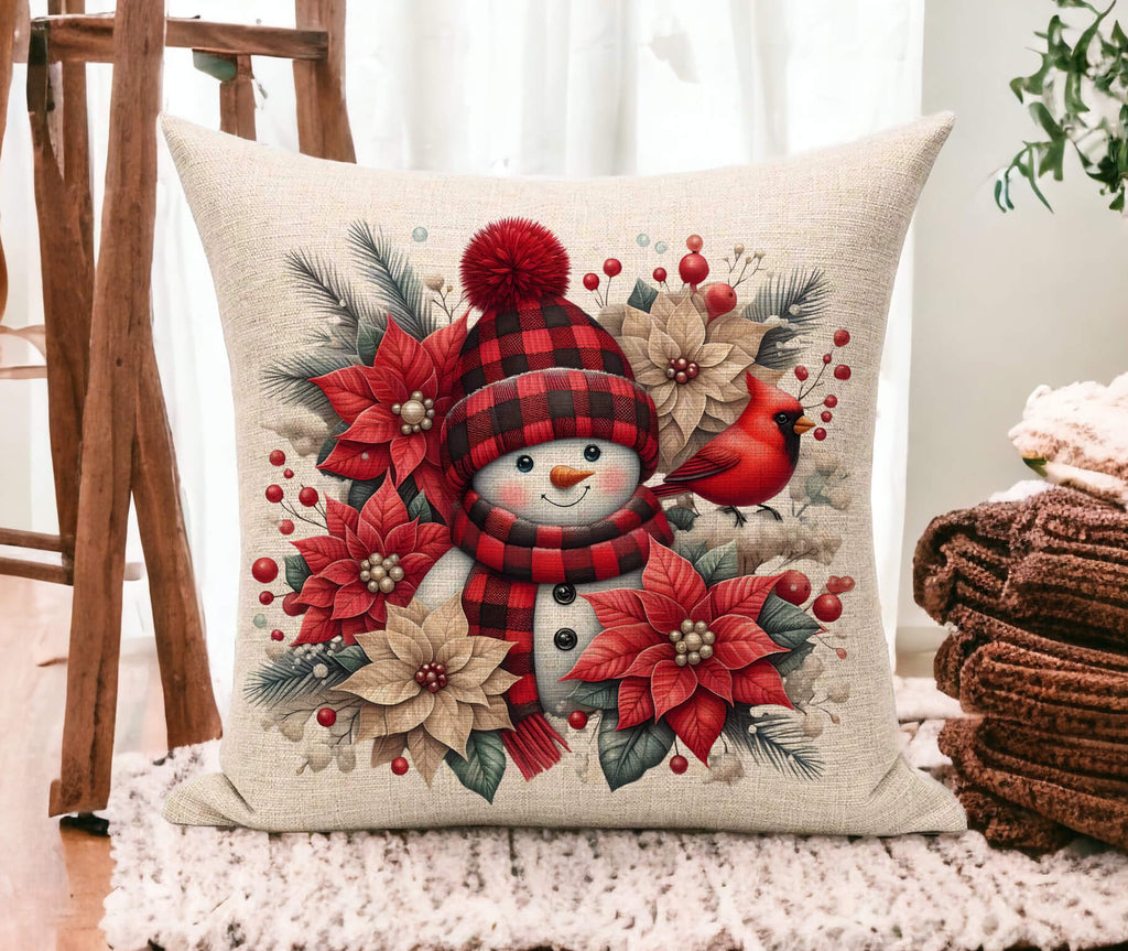 Decorative pillow with a snowman design featuring red and beige flowers, a cardinal, and a plaid hat on a neutral background.
