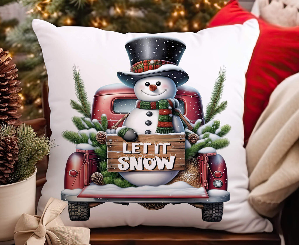 Decorative pillow with a Christmas design featuring a snowman and red truck, surrounded by festive decor.