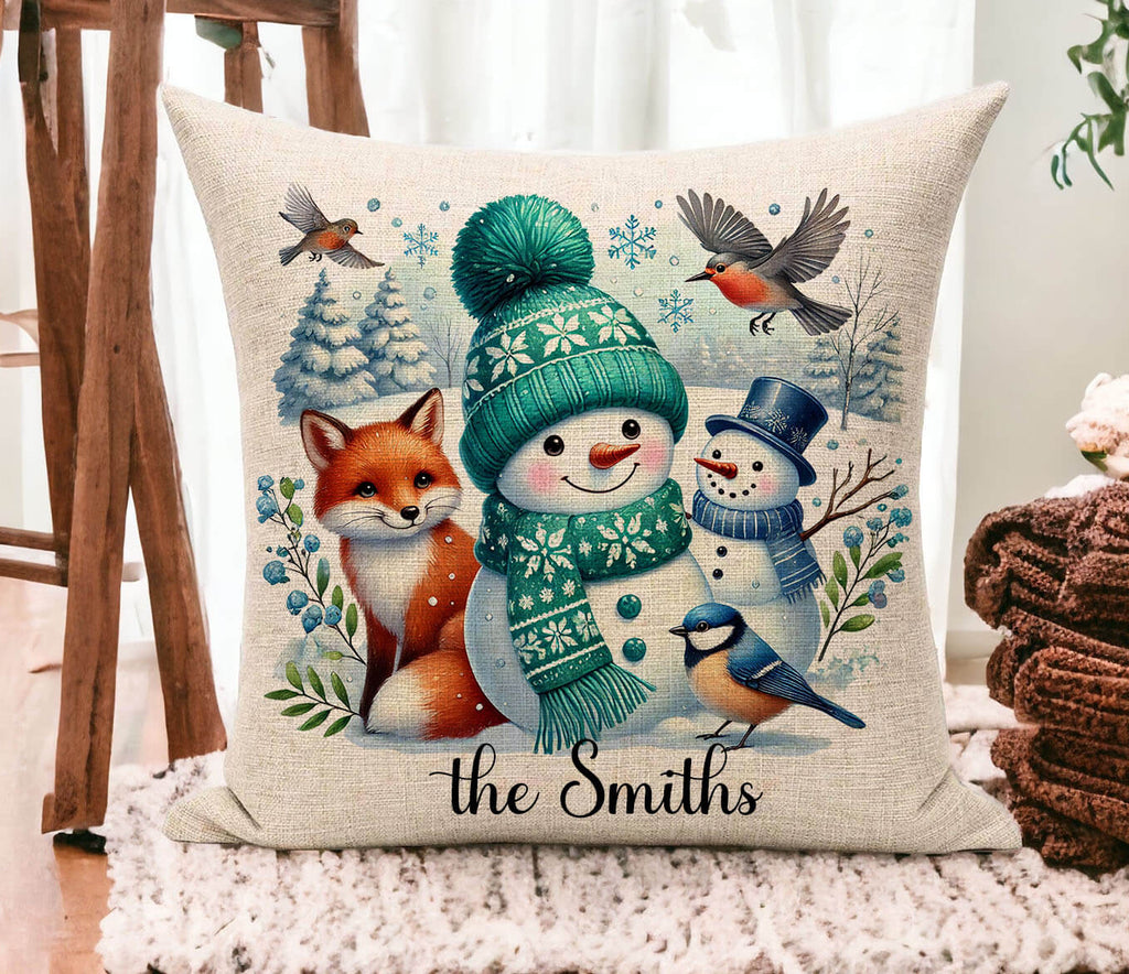 Decorative pillow with a snowman, fox, and birds design on a wooden floor.